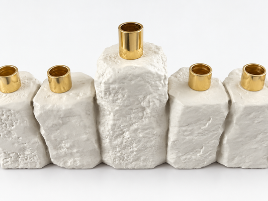 Close-up of the taller center shamash and gold-tone candle holders on the rough white concrete menorah.