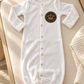 White Brit Milah baby gown with black and gold crown patch styled on ivory nursery linen