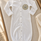 White Brit Milah baby gown with silver crown patch styled on ivory nursery linen