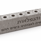 Close view of textured gray concrete hanukkiah and engraved Al Hanissim Hebrew inscription