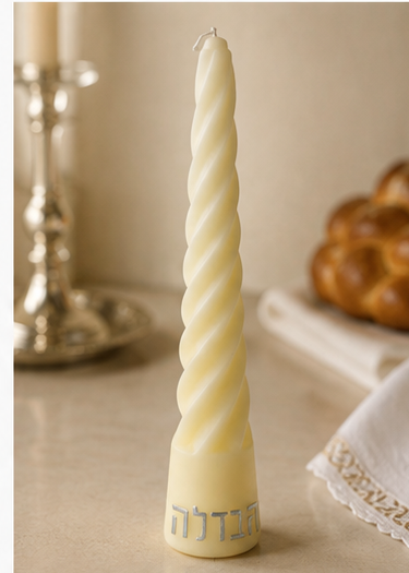Cream twisted Havdalah candle with silver Hebrew lettering staged on a warm Shabbat table