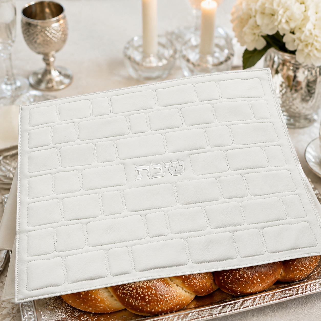 White Western Wall challah cover staged over challah on a Shabbat table