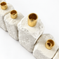Angled top detail showing open gold-tone candle holders and the rough white concrete texture.
